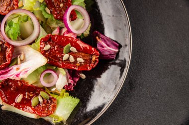 Salata, kurutulmuş domates, yeşil yaprak, soğan, doğal ürün, lezzetli aperatif. Lezzetli gurme yemek arkaplanı, masa, rustik üst manzara, fotokopi alanı, vejetaryen diyeti ve vejetaryen yemeği.