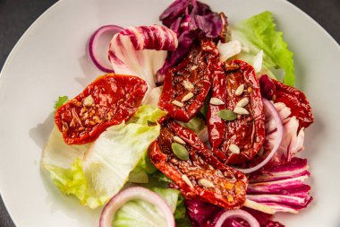 Salata, kurutulmuş domates, yeşil yaprak, soğan, doğal ürün, lezzetli aperatif. Lezzetli gurme yemek arkaplanı, masa, rustik üst manzara, fotokopi alanı, vejetaryen diyeti ve vejetaryen yemeği.