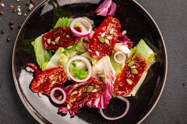 Salata, kurutulmuş domates, yeşil yaprak, soğan, doğal ürün, lezzetli aperatif. Lezzetli gurme yemek arkaplanı, masa, rustik üst manzara, fotokopi alanı, vejetaryen diyeti ve vejetaryen yemeği.