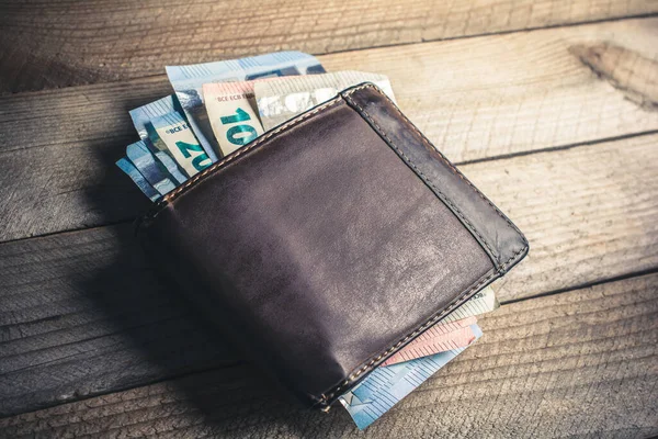 Tahta bir tahtanın üzerinde kahverengi bir cüzdan ve yüksek açılı bazı Euro banknotları görülüyor.