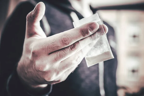 Att hantera droger av en man som håller i en liten påse med vitt pulver i handen Stockfoto
