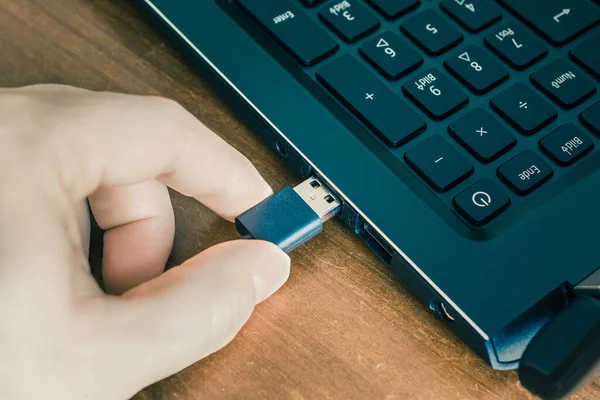 Männliche Hand verbindet ein schwarzes USB-Kabel mit dem USB-Port eines schwarzen Notebooks — Stockfoto