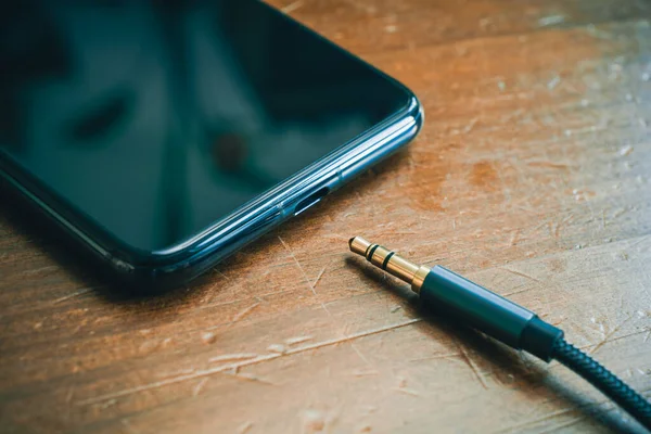 Koptelefoonkabel liggend voor een smartphone zonder koptelefoonaansluiting op houten tafel — Stockfoto