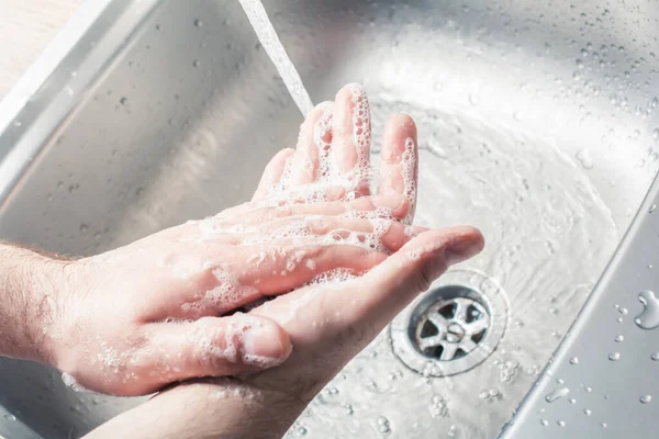 Männchen seift seine Hände neben dem Gießen von Wasser an einer Küchenspüle ein — Stockfoto