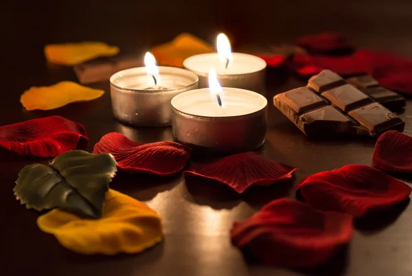 Romantische theelichten met chocolade en roze bloemblaadjes — Stockfoto