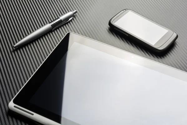 Smartphone de negocios en blanco y una pluma que yace junto a una tableta con reflexión sobre un fondo de carbono —  Fotos de Stock