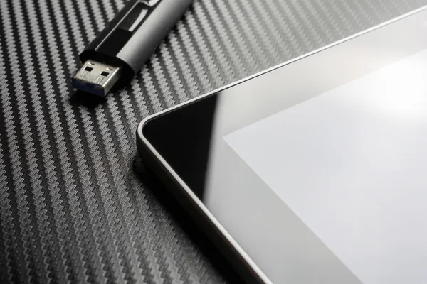 Unidade flash de armazenamento USB que jaz ao lado do tablet de negócios em branco com reflexão sobre o fundo de carbono — Fotografia de Stock
