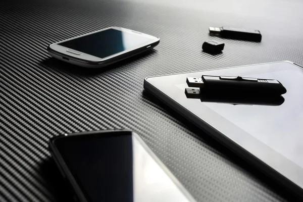 2 Business Mobiles With Reflections And An USB Drive Lying Next To A Blank Tablet With An USB Drive On Top, All Above A Carbon Layer — Zdjęcie stockowe