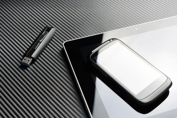 Smartphone en blanco con reflexión que se encuentra en la tableta de negocios junto a una unidad flash de almacenamiento USB sobre un fondo de carbono —  Fotos de Stock