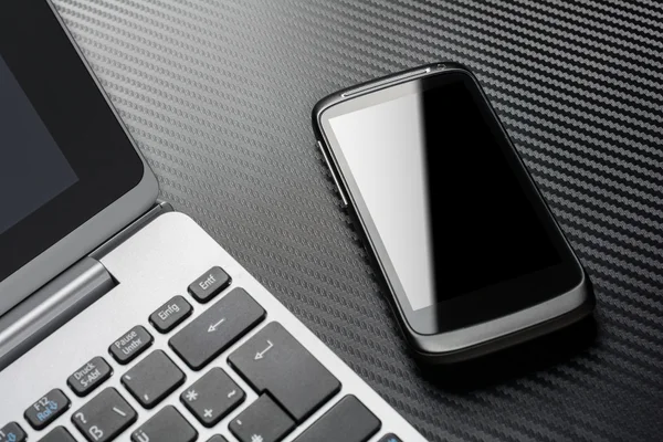 Business Work With Black Smartphone With Reflection Lying Right To A Notebook Keyboard, All Above A Carbon Layer — Stock Fotó