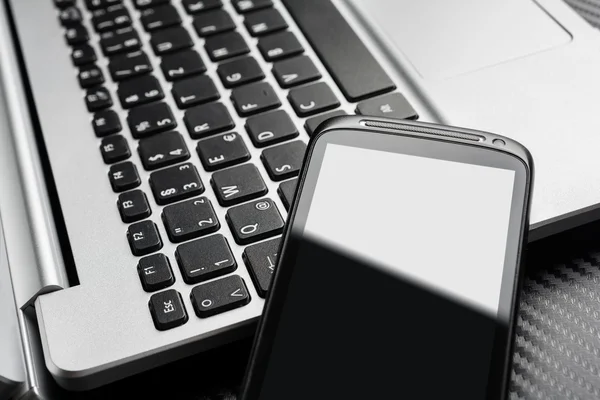 Smartphone de negocios negro en blanco con reflexión apoyada en un teclado portátil, todo por encima de una capa de carbono —  Fotos de Stock