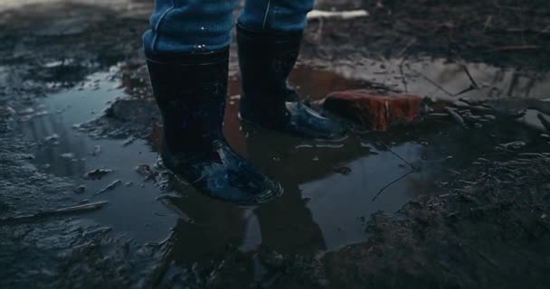 ゴム製のブーツを着た赤ん坊の女の子が水たまりに飛び込む 春の天気 融雪雪 路上で面白いゲーム 暖かい春の天気 4K選択フォーカス 女の子は彼女の頭を上げる — ストック動画