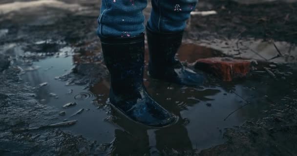 一个穿着橡胶靴的女婴跳进了水坑 春天的天气 融化的雪 街上有趣的游戏 温暖的春天天气 4K选择性聚焦 那女孩抬起头来 — 图库视频影像