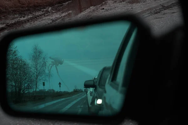 A rear-view mirror with an anti-reflective coating. Cars stand in a row, queue. In the background you can see a tripod unidentified robot that shines the headlight to the side. Rainy, foggy weather. Background