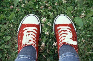 Red sneakers with white laces stand on the green grass. Rest in nature, exercise outdoors