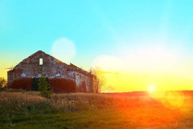 Sahada terk edilmiş kırmızı tuğladan bir bina duruyor. Gün batımında parlak güneş ışıldayan parlak ışınlarla parlar. Terk edilmiş tarım.
