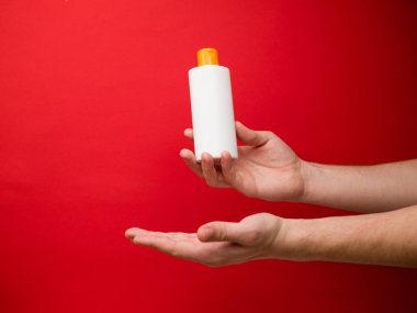 Kırmızı arka planda el ele tutulan şampuan şişesi..