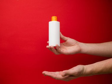 Kırmızı arka planda el ele tutulan şampuan şişesi..