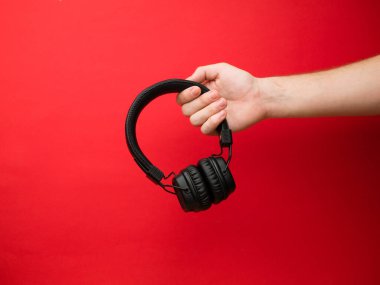 Genç bir kadın elinde bir çift siyah kablosuz kulaklık tutuyor. Kırmızı arka planda kulaklığı olan bir kızın eli..