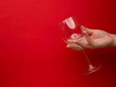 Kırmızı arka planda boş bir şarap kadehini tutarken. Kopyalamak için geniş kenarlı görünüm. Tatil geçmişi kavramı.