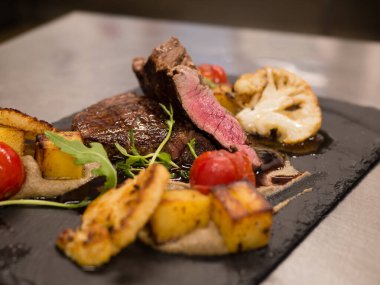 Lezzetli biftek, orta pişmiş, baharatlı ve ızgara sebzeli, siyah taş tabakta, yakın plan..