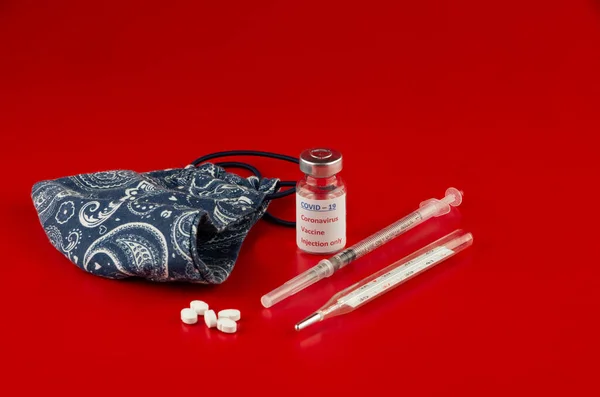 COVID için aşı - 19 Coronavirus, tıbbi termometre, haplar ve kırmızı arka planda ev yapımı yüz maskesi, hasta