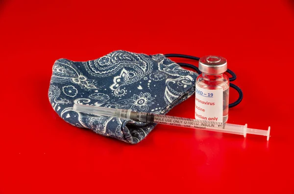 COVID için - 19 Coronavirus, tıbbi aşı ve kırmızı arka planda ev yapımı yüz maskesi.
