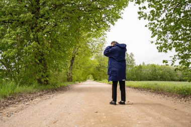 Mavi örgülü siyah pantolonlu adam yolda duruyor, çimen