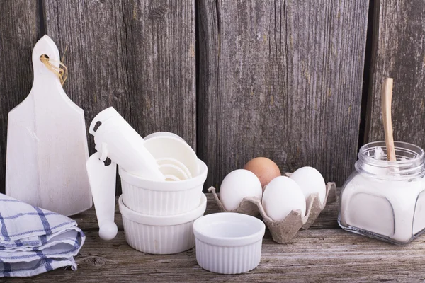 Bodegón en una mesa de madera de cocina con moldes de cerámica blanca para hornear, huevos, harina y otros utensilios —  Fotos de Stock