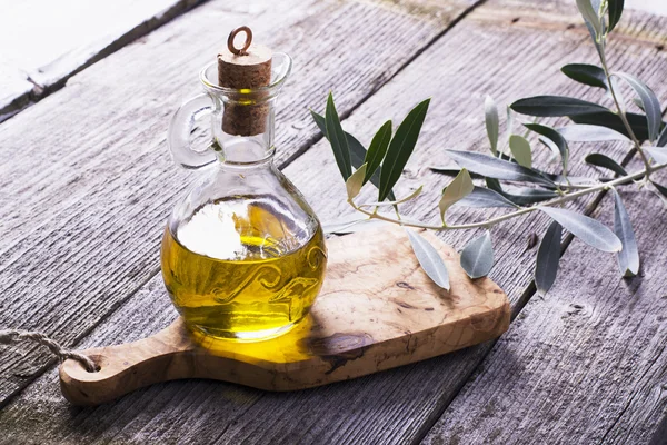 Jarra con aceite de oliva virgen extra sobre tabla de cortar rodeada de ramas —  Fotos de Stock