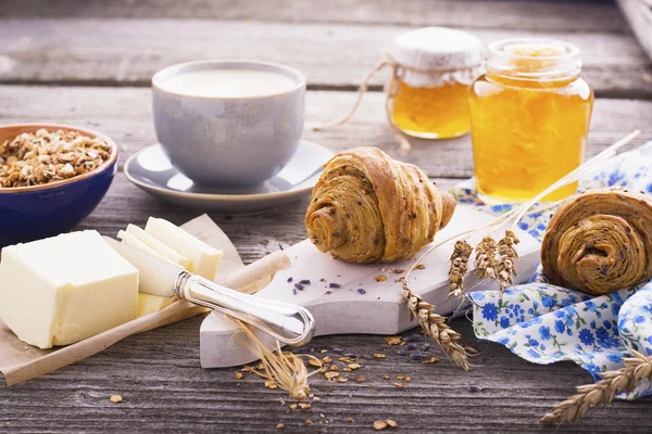 Café da manhã clássico com cereais, croissants e mel servido em um fundo de madeira em estilo rústico — Fotografia de Stock