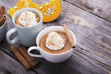 Mikrodalgada hızlı yemek kahvaltı atıştırmalık. Kokulu ev yapımı kabak pasta ahşap bir arka plan üzerinde krem şanti ve tarçın ile fincan porsiyonlarda beş dakika düşmek