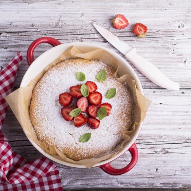 Ev Pazar pastası akşam yemeği için pudra şekeri, çilek dilimleri ve taze nane yaprakları, fesleğen ile dekore edilmiştir. Hafif ahşap vintage masa örtüsü el yapımı bir seramik kırmızı arka plan pişirme servis.