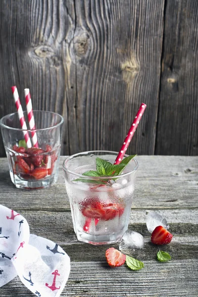 Bicchiere di acqua ghiacciata rinfrescante con fette succose fragole mature, foglie di menta e cubetti in un semplice fondo di legno. Il concetto di vacanza estiva relax. focus selettivo — Foto Stock