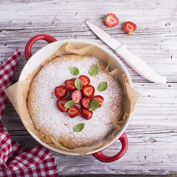 Ev Pazar pastası akşam yemeği için pudra şekeri, çilek dilimleri ve taze nane yaprakları, fesleğen ile dekore edilmiştir. Hafif ahşap vintage masa örtüsü el yapımı bir seramik kırmızı arka plan pişirme servis.