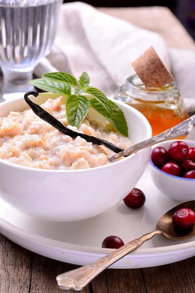 Hot homemade milk oatmeal with natural vanilla and organic cranberries in a white ceramic bowl — Stock Photo, Image