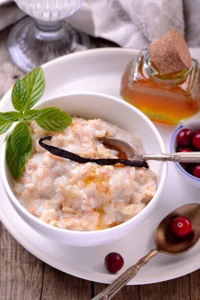 Hot homemade milk oatmeal with natural vanilla and organic cranberries in a white ceramic bowl — Stock Photo, Image