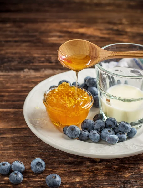 Mirtilli da giardino con un bicchiere di latte fresco e favi — Foto Stock