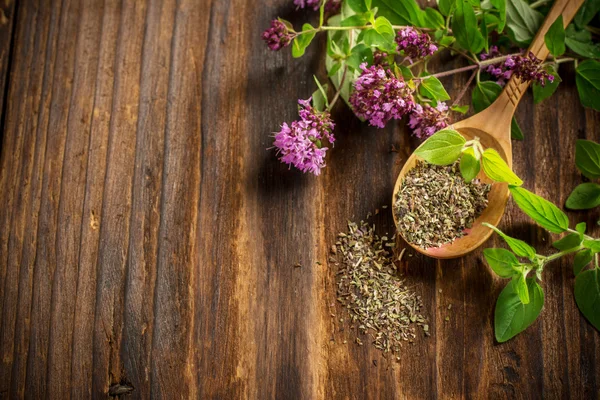 Dried oregano in a wooden spoon and twigs of fresh green  with flowers — Stock Photo, Image