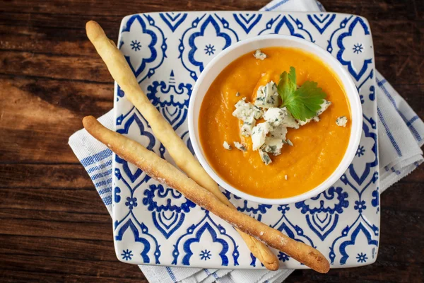 Cream of pumpkin soup with blue cheese and homemade grissini bread sticks in a white bowl — Stock Image Cream of pumpkin soup with blue cheese and homemade grissini bread sticks in a white bowl Stock Picture