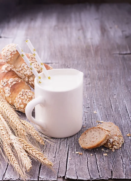 Tasse avec lait pour le petit déjeuner et des oreilles de baguettes de pain maison fraîches — Photo