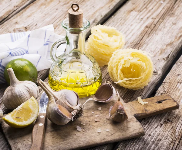 Kitchen simple still life of pasta, olive oil, fresh garlic, herbs and grasses — Stockfoto