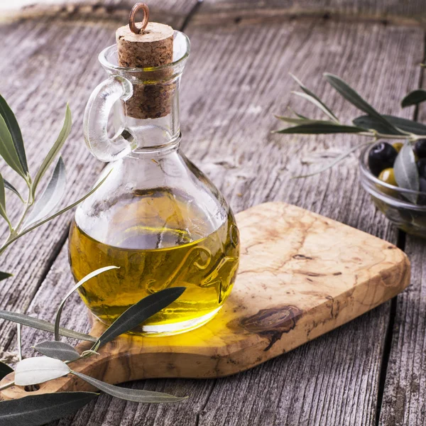 Jarra con aceite de oliva virgen extra sobre tabla de cortar rodeada de ramas —  Fotos de Stock