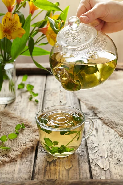 Melissa tea healthy beverage drops from teapot in cup — Stock Photo, Image