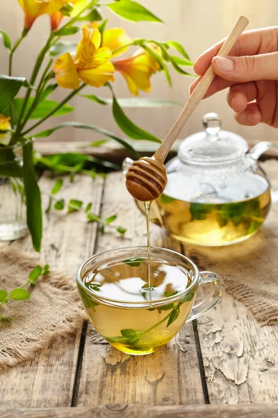 Peppermint tea with honey in glass cup, teapot and flowers — Stok fotoğraf