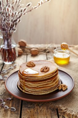 Stack of pancakes with flowing honey and nuts on table