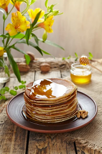 Pancakes with flowing honey and flowers on vintage wooden table — Stock Photo, Image