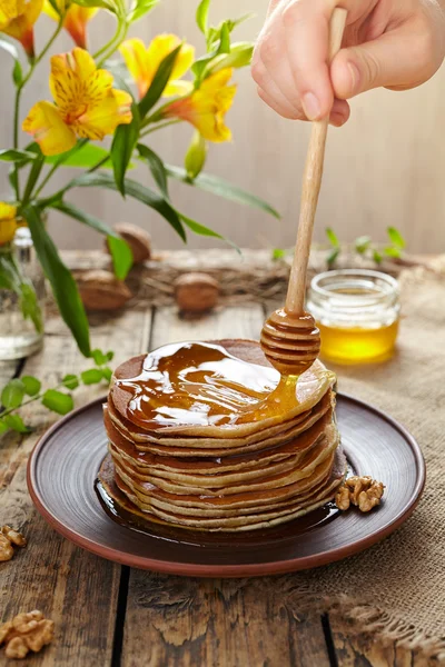 Honig auf einem Stapel traditioneller hausgemachter Pfannkuchen mit Nüssen verteilen — Stockfoto