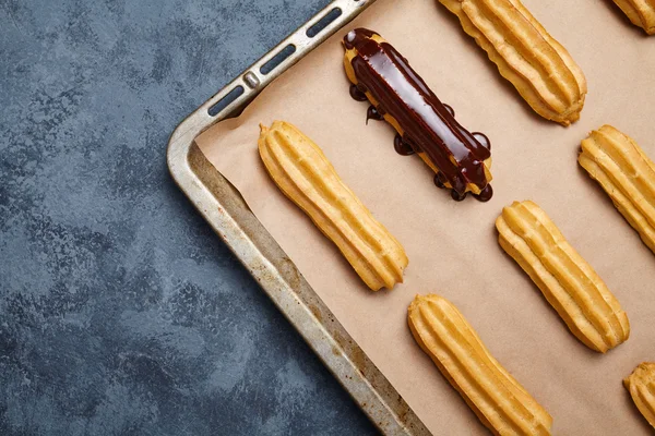 Eclairs o profiterole con la preparación del chocolate en la bandeja de hornear —  Fotos de Stock