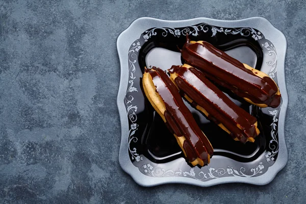 Eclairs o profiteroles con cioccolato e panna montata su piatto Foto Stock